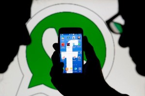 An illustration photo shows a man holding a smart phone with a Facebook logo as its screen wallpaper in front of a WhatsApp messenger logo, in Zenica February 20, 2014. Facebook Inc will buy fast-growing mobile-messaging startup WhatsApp for $19 billion in cash and stock in a landmark deal that places the world's largest social network closer to the heart of mobile communications and may bring younger users into the fold. REUTERS/Dado Ruvic (BOSNIA AND HERZEGOVINA - Tags: SCIENCE TECHNOLOGY BUSINESS TPX IMAGES OF THE DAY)